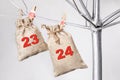 Two matting bags for gifts with numbers 23 and 24 hanging on silver tree. 23, 24 - advent calendar.