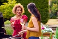 Two Mature Female Friends Cooking Outdoor Barbeque And Drinking Wine At Home Royalty Free Stock Photo