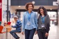 Two Mature Female Students Or Teachers Walking Through Communal Hall Of Busy College Campus Building