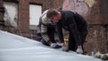 Two mature guys fixate grey tarpaulin to dome with white plastic loop pins.