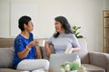 Two mature middle-aged Asian women are enjoying their morning coffee and talking on a sofa Royalty Free Stock Photo