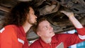 Two mechanic Caucasian man in large garage, Inspecting parts under raised car come in repair problematic part, male mechanic