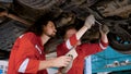 Two mechanic Caucasian man in large garage, Inspecting parts under raised car come in repair problematic part, male holding laptop