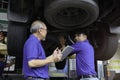 Two mechanic checking wheel and inspecting car under body and suspension system at garage  technician check and repair customer Royalty Free Stock Photo