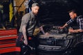 Two mechanics fixing car`s engine in a garage. Royalty Free Stock Photo