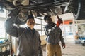 Two mechanics working under a lifted car using tools in a modern car repair shop Royalty Free Stock Photo