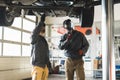 Two mechnics during work. One holding a flashlight, another inspecting car's bottom Royalty Free Stock Photo