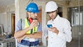 Two men builders and architect using smartphone drinking coffee at construction site