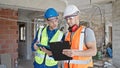 Two men builders reading document using touchpad shake hands at construction site