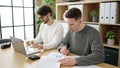 Two men business partners using laptop writing on document working at office Royalty Free Stock Photo