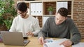 Two men business partners using laptop writing on document working at office Royalty Free Stock Photo