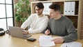 Two men business partners using laptop writing on document working at office Royalty Free Stock Photo