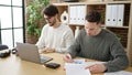 Two men business partners using laptop writing on document working at office Royalty Free Stock Photo