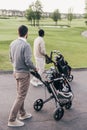 Two men carrying golf clubs in golf bags and walking at golf course Royalty Free Stock Photo