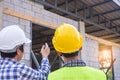 Two men on construction site wearing hard hats. Standing and talking about the problems of house construction