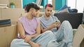 Two men couple using smartphone sitting on floor at new home Royalty Free Stock Photo