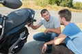 two men crouching to look at rear parked motorcycle