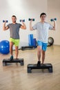 Two men doing step aerobic exercise with dumbbell on stepper Royalty Free Stock Photo