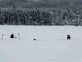 Two men fishing from the ice of a frozen lake covered in deep snow