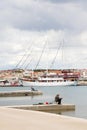 Two men fishing on a seaside pier, a sailing ship behind them