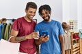 Two men friends holding shopping bags using smartphone at clothing store Royalty Free Stock Photo