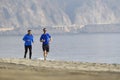 Two men friends running together on beach sand coast mountain bachground in healthy lifestyle concept Royalty Free Stock Photo