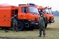 Two men in gas mask and special safe suit for biological danger in front of the orange lorries. Field on background