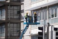 Two men in hard hats cleaning tall building windows using hydraulic lift