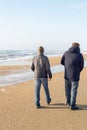 Two men in jackets are walking along the sandy beach on a sunny winter day. Lifestyle and travel Royalty Free Stock Photo