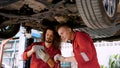 two men are mechanics, working in large garage, two mechanics checking undercarriage car raised high see lower part clearly, Royalty Free Stock Photo