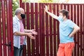 Two men in medical mask speaking to each other, discuss problems on sunny day