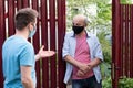 Two men in medical mask speaking to each other, discuss problems on sunny day