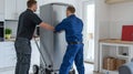 Two men moving a large refrigerator in a modern kitchen. Home relocation service in action. Efficient, professional Royalty Free Stock Photo