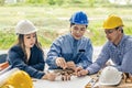 Two man one women architect draws a plan,on large sheet of paper at office desk and builds model house from wooden blocks bars. Royalty Free Stock Photo