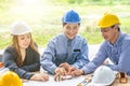 Two man one women architect draws a plan,on large sheet of paper at office desk and builds model house from wooden blocks bars. Royalty Free Stock Photo