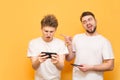 Two men play games on smartphones, isolated on a yellow background. Man laughs at a friend, another loser and frustrated. Two