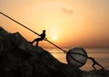Two Men Pulling and Pushing Uphill A Big Rock Together With a Metal Chain In Front Of Beach Sunrise Royalty Free Stock Photo