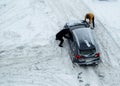 Two men push out a car stuck in the snow. The car skids in a snowdrift on an icy road. Uncleaned roads from snow. Copy space for Royalty Free Stock Photo