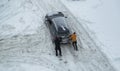 Two men push out a car stuck in the snow. The car skids in a snowdrift on an icy road. Uncleaned roads from snow. Copy space for Royalty Free Stock Photo