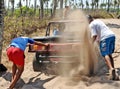 Two men pushing a buggy jammed in the sand.