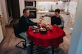 Two men share a casual dinner at a red tablecloth table in a cozy home kitchen Royalty Free Stock Photo