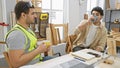 Two men sharing a break in a luminous carpentry workshop, surrounded by wooden frames and tools Royalty Free Stock Photo
