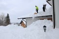 Two men shoveling high, heavy snow from a house roof