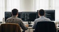 Two software developers working together on multiple computer screens with programming code displayed Royalty Free Stock Photo