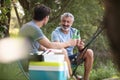 two men sitting by river fishing and holding beers