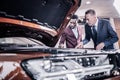 Two men standing near brown hatchback car with opened front trunk