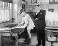 Two men standing in an office, one ironing his pants Royalty Free Stock Photo