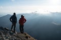 Two men standing standing with trekking poles on cliff edge and looking at sunset rays over the clouds. Successful summit concept Royalty Free Stock Photo