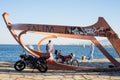 Two Men Talking at Waterfront beside Sculpture of Ship Skeleton