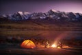 Two men tourists sitting at the illuminated tent near campfire